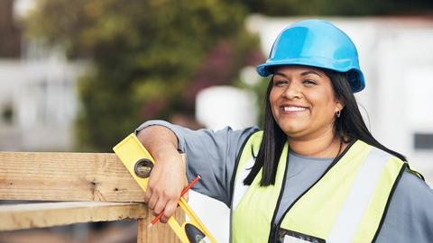 A woman contractor wearing a safety vest holds a level on a jobsite.